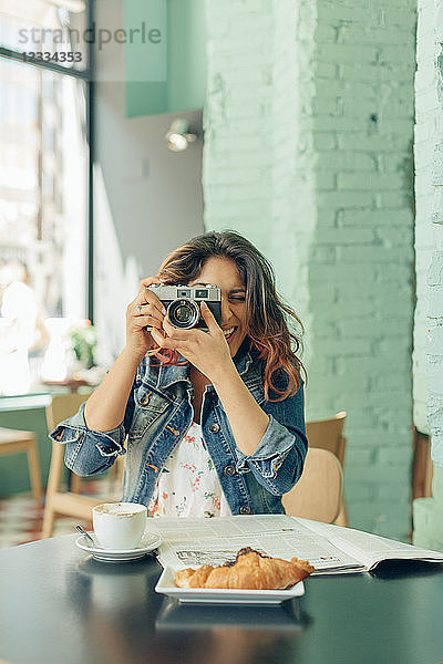 Laughing woman sitting at coffee shop taking pictures with camera