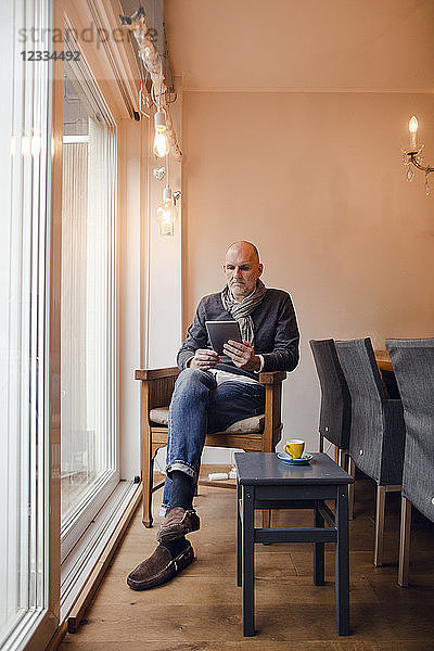 Senior man sitting at home  reading on digital tablet