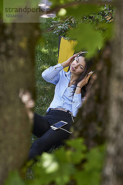 Young woman sitting on a meadow listening music with headphones and cell phone