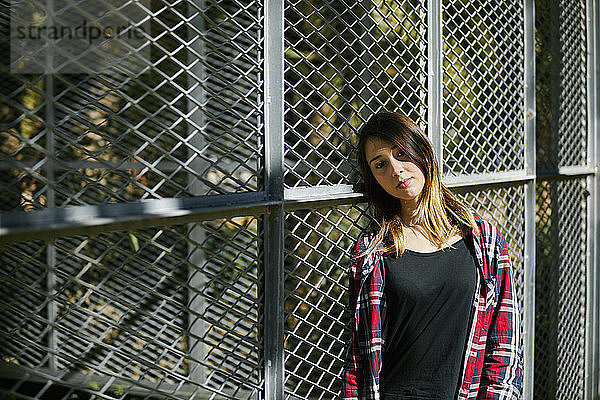 Portrait of beautiful young woman leaning against a fence