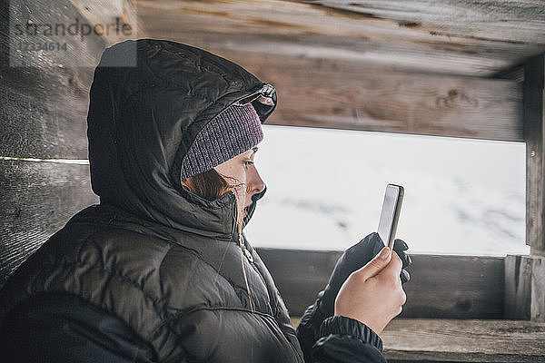 Austria  Kitzbuehel  young woman in raised hide looking at cell phone in winter