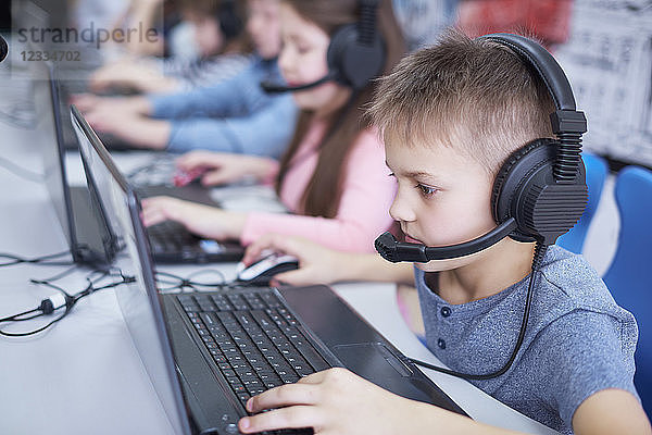 Pupils wearing headsets and using laptops in school