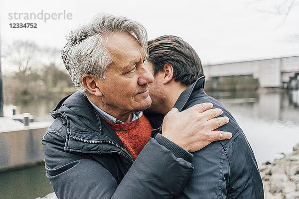 Young man and senior man embracing at the riverside