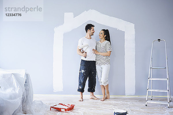 Happy couple painting in new apartment with house shape on wall