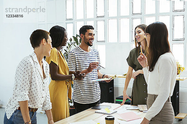 Smiling colleagues working together at desk in office discussing papers