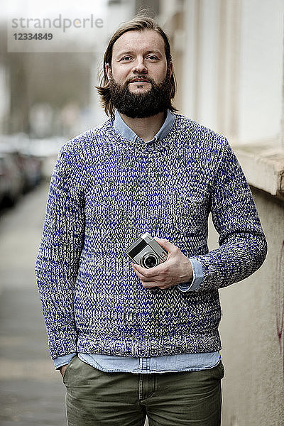 Man with beard standing in street  holding old camera