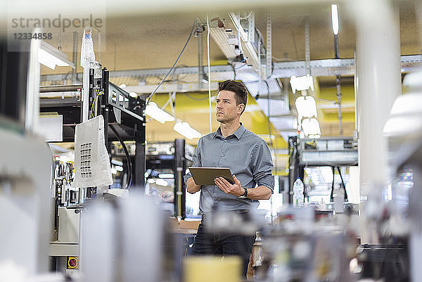 Man standing in factory with tablet looking sideways