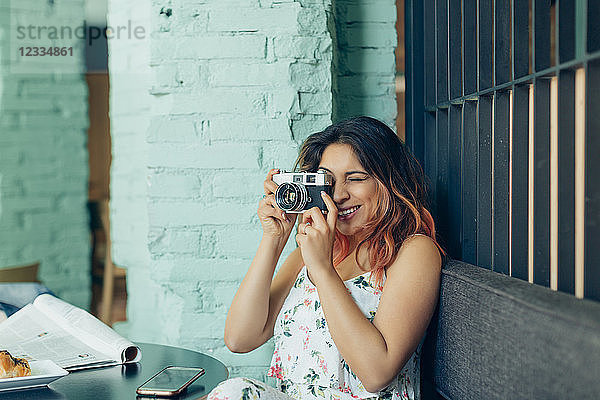Smiling woman sitting in coffee shop taking pictures with camera