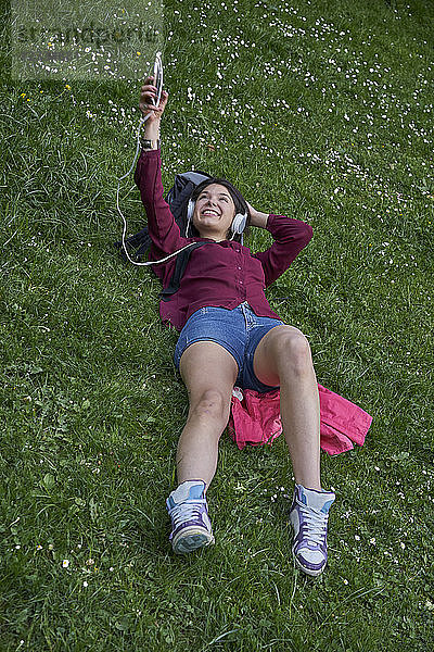 Young woman lying on a meadow listening music with headphones and cell phone