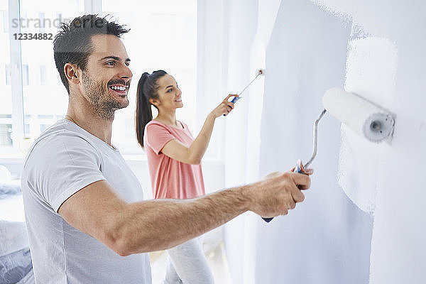 Happy couple painting wall in apartment together