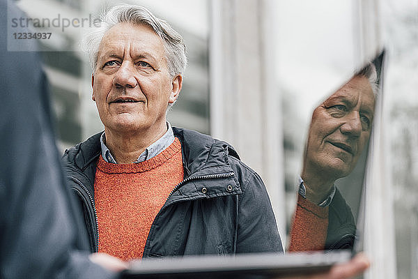 Senior man looking at man holding laptop outdoors