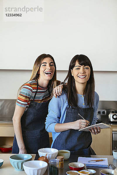 Portrait of two happy women with notebook in kitchen