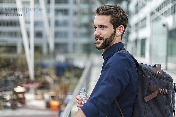 Smiling young businessman with backpack and bottle of water outdoors
