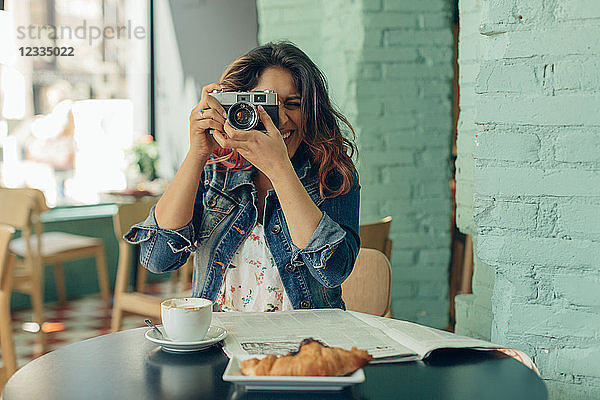Laughing woman sitting in coffee shop taking pictures with camera