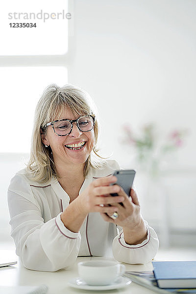Laughing mature businesswoman looking at cell phone at desk