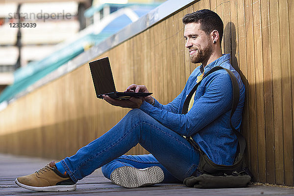 Young man sitting on footbridge using laptop