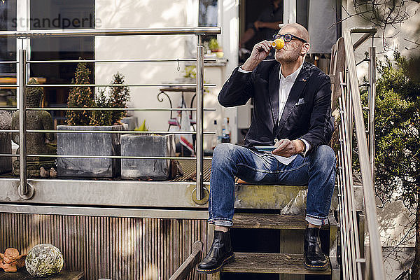 Senior man sitting on stairs of his patio  drinking coffee