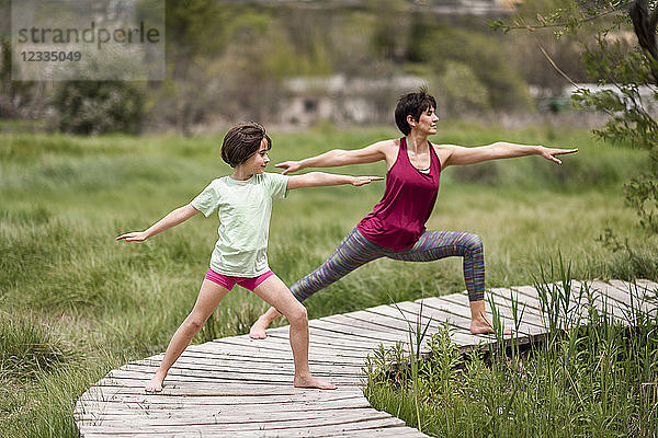 Mother and daughter doing yoga on boardwalk
