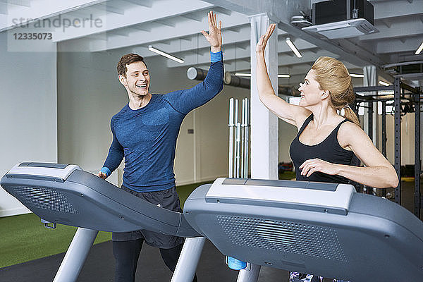 Happy man and woman doing high five during treadmill exercise at gym