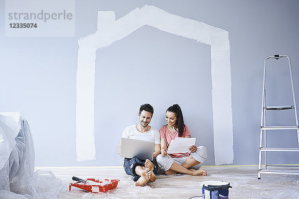 Couple sitting in new apartment using laptop