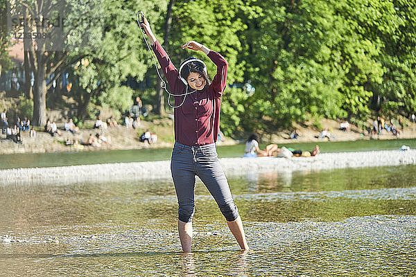Happy young woman listening music with headphones and cell phone dancing at riverside