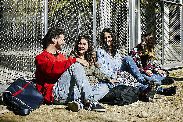 Four happy friends sitting at fence talking