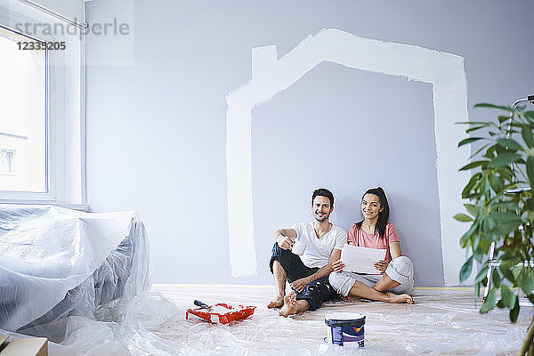 Happy couple taking break from painting walls in new apartment