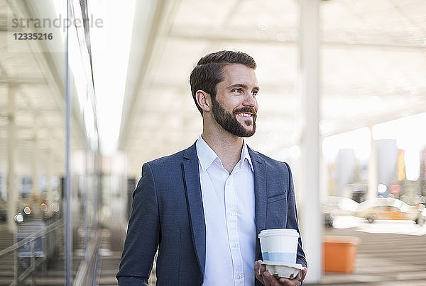 Smiling young businessman holding tray with takeaway coffee