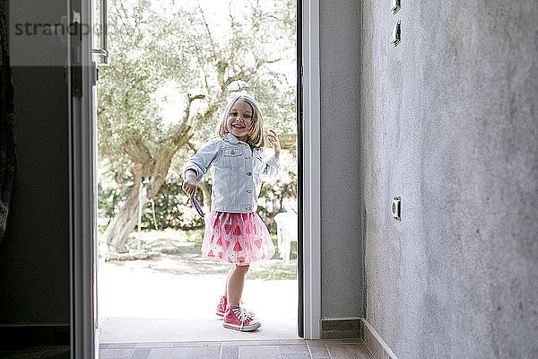 Portrait of laughing little girl standing in front of open entry door