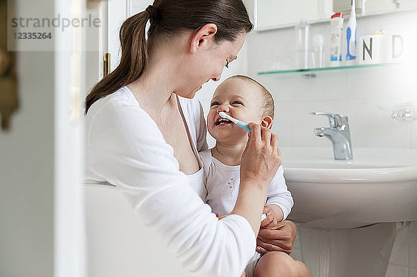 Mother brushing baby's teeth in bathroom