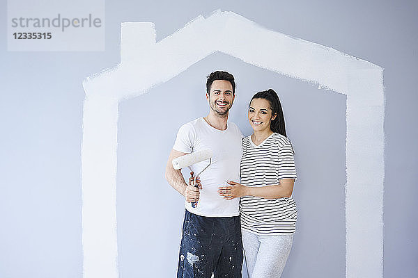 Portrait of happy couple painting in new apartment with house shape on wall