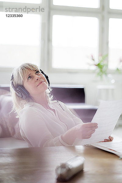 Relaxed mature businesswoman wearing headphones at desk looking up
