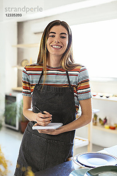 Portrait of smiling woman with notebook in kitchen