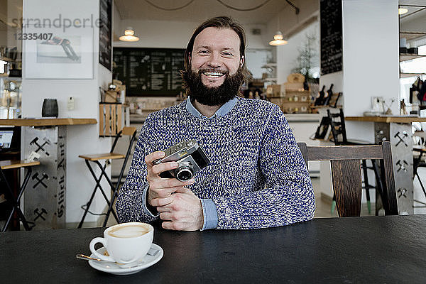 Man with beard sitting in cafe  holding old camera