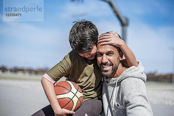 Portrait of happy father and son with basketball outdoors