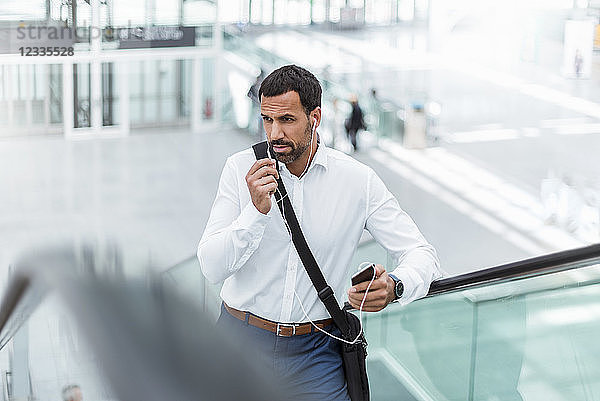 Businessman using smartphone  earphones  on escalator