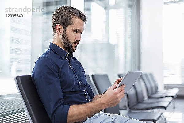 Young businessman sitting in waiting area using tablet