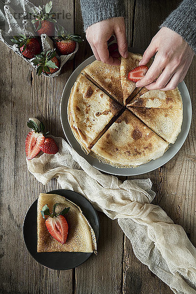 Hands of young woman preparing pancakes for breakfast with strawberries