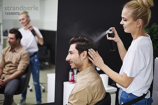 Smiling hairdresser using hairspray on man's hair