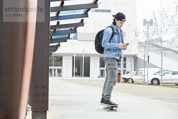 Young man skateboarding in the city  using smartphone  listening music