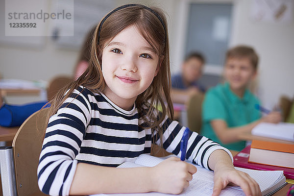 Portrait of smiling schoolgirl writing in exercise book in class