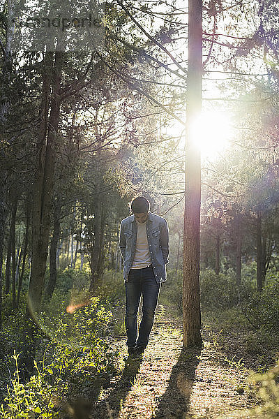 Young man standing in forest  against the sun