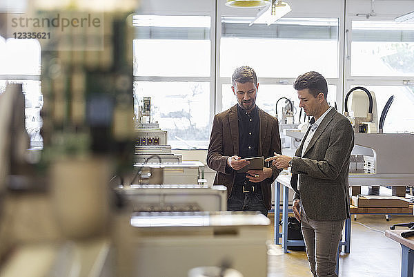 Two businessmen with tablet talking in factory
