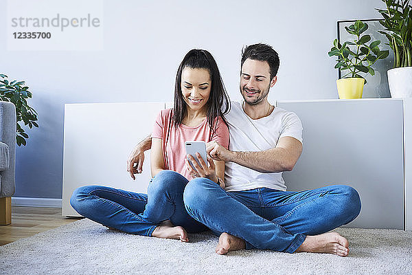 Couple sitting on floor and using smartphone