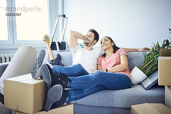 Happy couple sitting on couch surrounded by cardboard boxes