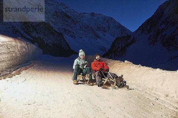 Couple sledding in snow-covered landscape at night
