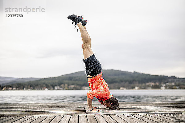 Athlete doing a headstand on wooden deck at the lakeshore