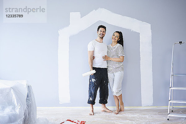 Portrait of happy couple painting in new apartment with house shape on wall