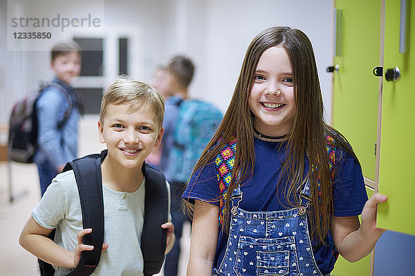 Portrait of smiling schoolboy and schoolgirl at lockers in school