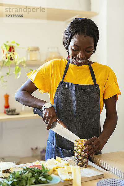 Smiling woman cutting pineapple in kitchen